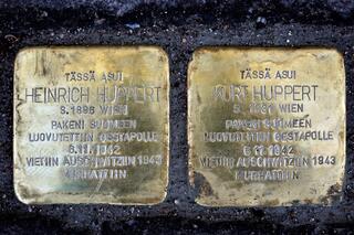 Kaksi metallilaattaa asfaltissa. Niissä tekstit: Tässä asui Heinrich Huppert s 1896 Wien Pakeni Suomeen Luovutettiin Gestapolle 6.11.1942 Vietiin Auschwitziin 1943 Murhattiin