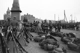 Saksalaisia sotilaita kauppatorilla. Maassa on varustekasoja ja kiväärejä on aseteltu nippuihin.