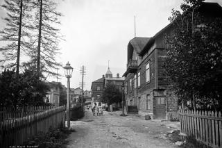 Katunäkymä Länsi-Pasilassa vuonna 1912. Kuvassa on työväen asuntoja suurempi puuhuvila. Hiekkatiellä kävelee muutama ihminen.