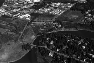 Flygbilden visar Tammelunds våningshus i förgrunden. Längre bort syns åkrar och industribyggnader. Landskapet korsas av landsvägar.