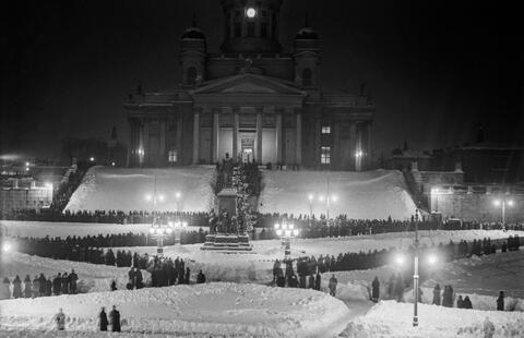 Uudenvuoden viettoa Senaatintorilla Helsingissä 31.12.1931. Ihmiset seisovat korkeiden lumikinosten sekaan auratuilla käytävillä.