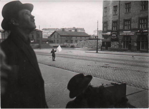 En ung man bär en vit flagga på Broholmsgatan. I förgrunden två män som tittar snett uppåt. 