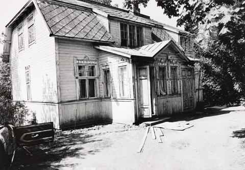 Mansardikattoisen puurakennuksen vieressä on purkujätettä.
