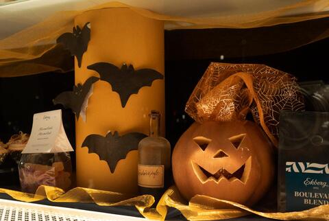 Näyteikkuna on somistettu halloween-koristeilla ja myynnissä olevilla tuotteilla. Vasemmalla pussi Ekbergin marmeladia ja sen vieressä pylväs, jossa on lepakkokoristeita. Oikealla Ekbergin kahvipaketti ja sen vieressä kurpitsakoriste.