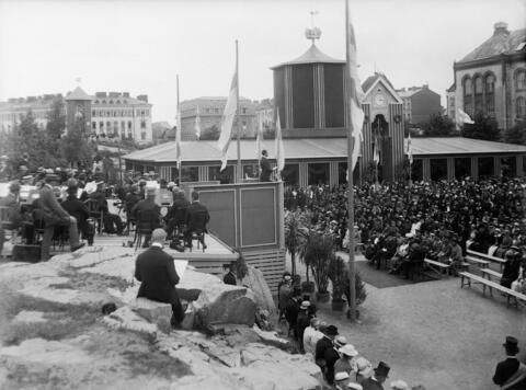 Ensimmäiset Suomen messut vuonna 1920 Punanotkonpuistossa (nyk. Johanneksenpuisto). Näyttelijä Urho Somersalmi lausuu avajaisissa juhlarunon. Puhujakorokkeen edessä on korkeita ruukkukasveja ja sitten penkkirivejä, jotka ovat melkein täynnä yleisöä.  Puhujakorokkeen takana on lava, jolle on asettunut orkesteri. Lipputankoja on pystytetty useita, ja niissä liehuvat Suomen liput. Juhlapaviljongin taustalla vasemmalla kallion nyppylällä on messuja juhlistava toinen rakennus. Laivurinrinne 2, Merimiehenkatu 11