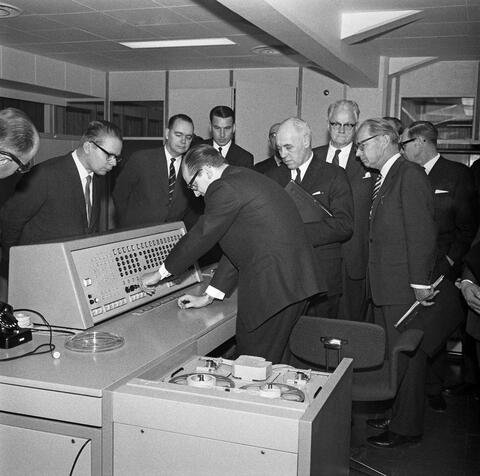 Tietokone Suomen kaapelitehtaalla Helsingissä joulukuussa 1961. Insinööri W. Raibl Siemensiltä esittelee uutta tietokonetta. Vakuutustarkastaja, tri T. Pentikäinen koneen takana vasemmalla, Kaapelitehtaan tj. Björn Westerlund ja ministeri Ilmari Hustich oikealla.