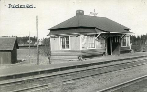 Pieni, yksikerroksinen puinen asemarakennus radan vieressä. Katolla on kyltti BOXBACKA.