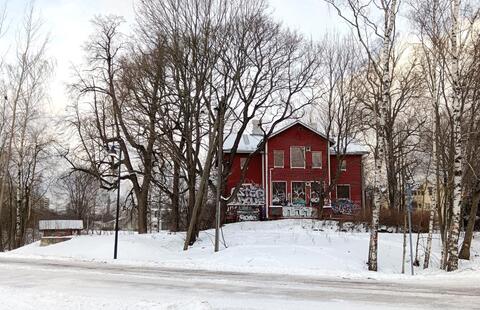 Punaiseksi maalattu ränsistynyt puuhuvila, jonka ikkunat on peitetty vanerilevyillä ja seinät töhritty.