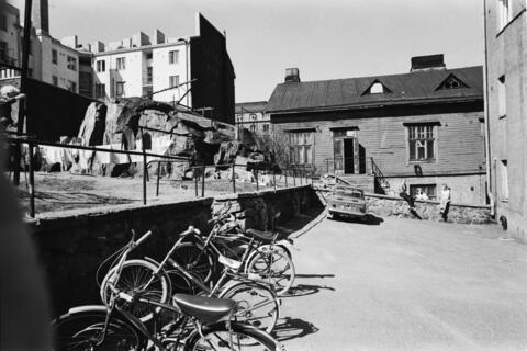 Näkymä Fleminginkatu 14:n pihalta. Etualalla polkupyöriä, taaempana Fleminginkatu 16:n puutalo ja kallio. Taustalla kerrostaloja.