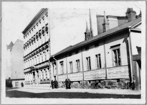 Ett fyravåningars stenhus som har bredvis sig ett lågt trähus med putsad fasad