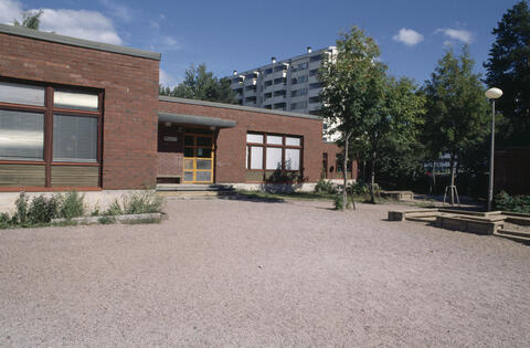 Matala punatiilinen rakennus, etualalla hiekkakenttää.