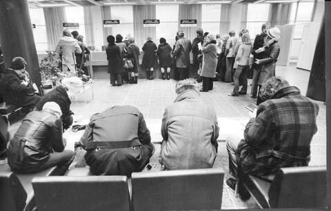 Merihaan verotoimistossa 7.1.1975. Kuvassa etualalla on neljä ihmistä selin kuvaajaan kumartuneina täyttämään lomakkeita. Taustalla on ihmisiä asiointitiskin ääressä tai jonottamassa tiskille.