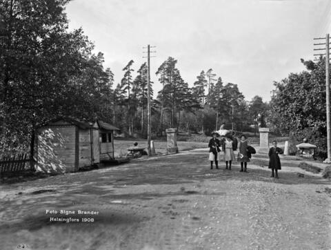 Kaupungin raja, Vanha tulliportti. Läntinen Viertotie 80 (nykyinen Mannerheimintie 108). Neljä lasta seisoo keskellä tietä, taustalla näkyy hevosella ratsastava mies. Tien vasemmalla puolella on matala puumökki, jonka takana tien kummallakin puolella on kivipaadet, joiden päällä tullinpuomi on aikoinaan levännyt.