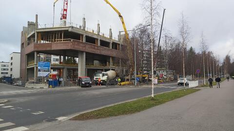 Alueella näkyy työmaaparakkeja, nostureita, pakettiautoja, rakennusmiehiä ja betoniauto. Myllypurontie kulkee kuvassa etualalla, Kiviparintie vasemmassa laidassa. Paikalla sijaitsi aiemmin Teboil-huoltoasema.