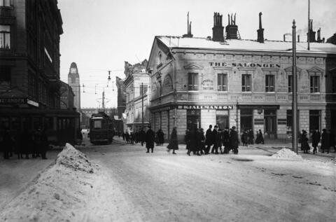 Raitiovaunuja kääntymässä Aleksanterinkadulta Keskuskadulle. Oikealla Aleksanterinkatu 17, jossa B. Kjällmanssonin tupakkakauppa ja sen yläkerrassa Thé Salongen.