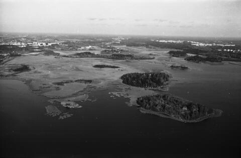 Viistoilmakuva pienlentokoneesta Kulosaaren suunnalta pohjoiseen yli Vanhankaupunginselän. Keskellä Kuusiluoto ja Lammassaari. Taustalla Viikki.