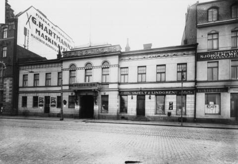 Keskellä on kaksikerroksinen empirerakennus, jonka sisäänkäynnin yläpuolella lukee VICTOR EK. Katutason liikehuoneistossa toimii SKEPPSFOURNERARE HJELT & LINDGRÉN SHIPCHANDLER.