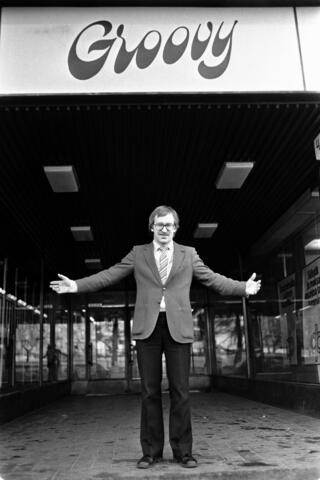 Mies seisoo kädet sivuille levitettyinä ravintolan sisäänkäynnin edessä. 