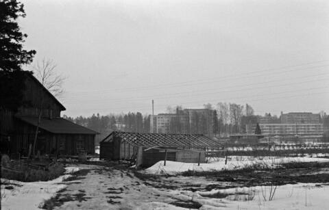 Lumisessa maisemassa vanhoja puurakennuksia ja taustalla elementtikerrostaloja.