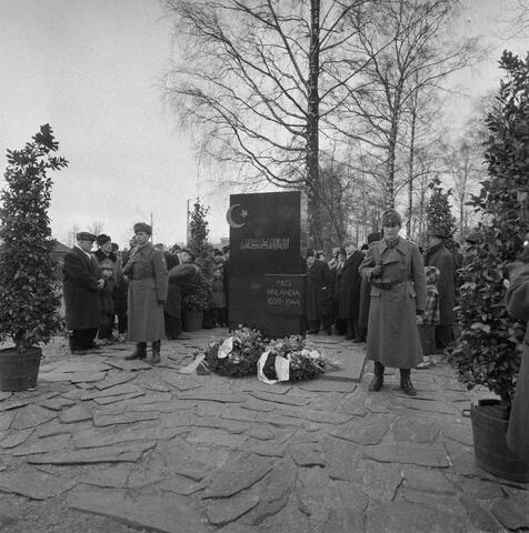 Soldater och civila har samlats vid ett minnesmärke som omges av skifferstenar.