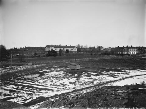 Etualalla tyhjää tonttia, taustalla matalia puurakennuksia.