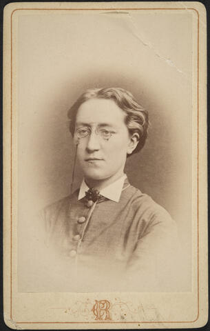 Rintakuva naisesta, jolla on kaulaan asti napitettu puku ja nenälasit.