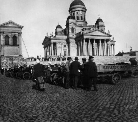 Ryhmä miehiä tarkastelee Senaatintorille kerättyjä ajoneuvoja. Taustalla tuomiokirkko.