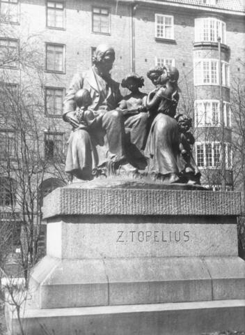 Veistos kuvaa istuvaa Topeliusta, jonka ympärillä on viisi lasta.