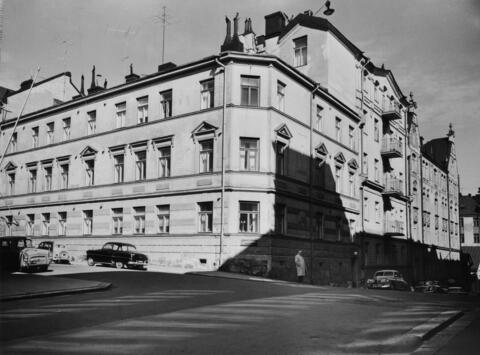 Kolmikerroksinen kivirakennus kuvattuna 2.5.1961. Kadulla on autoja ja jokunen jalankulkija.