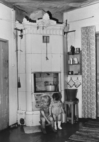 Kaksi pientä lasta hellakakluunin edessä.