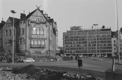 Byggnaden revs kort efter att bilden tagits, och Cirkelhuset stod klart på platsen år 1968. Två förbipasserande har stannat för att titta på bygget av Berghälls ämbetshus, som pågår i förgrunden. Till höger syns Postsparbankens byggnad på Sparbankskajen 2.