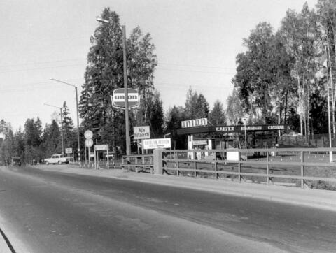 Tien toiselta puolelta vinottain kuvattu matala, laatikkomainen huoltoasemarakennus, jonka katolla ja pihalla on valomainos, jossa lukee union. Tasakaton sivustalla lukee CALTEX Mobiloil ja CASTROL.