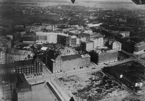 Främre Tölö, flygbild mot Helsingfors domkyrka (= Storkyrkan). I förgrunden Runebergsgatan 24, nuvarande Samposkvären och Kolerabarackerna. Runebergsgatan 33a, 31, 29, 27, 25, 23 (tom tont), 21. Tempelplatsen 8 (under konstruktion), 6, 4, 2.