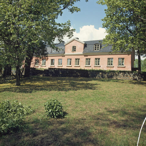 En ljusrosa karaktärsbyggnad i två våningar fotograferad på sommaren.