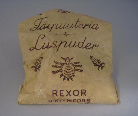Vitt luspuderpulver i en beigefärgad liten pappersförpackning. Förpackningen är öppnad och bär texten Täipuuteria Luspuder REXOR H:KI H:FORS