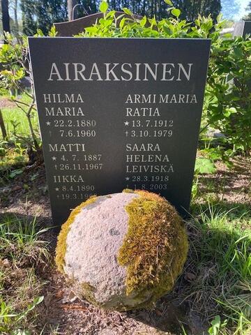 Mustassa yksinkertaisessa graniittipaadessa lukee AIRAKSINEN ja sen alla oikealla ARMI MARIA RATIA s. 13.7.1912, k. 3.10.1979