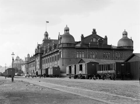 A huge brick building with train cars and railway tracks in front of it