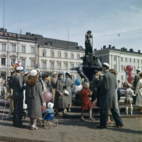 Aikuisia ja lapsia kokoontuneena Havis Amandan ympärille. Joillakin on ylioppilaslakki, joillakin kädessään ilmapallo.
