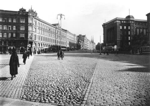 Oikealla Erottajankatu 19, 17–15, 13, 11. Vasemmalla Erottajankatu 4. Mukulakiviaukiolla kävelee ihmisiä.