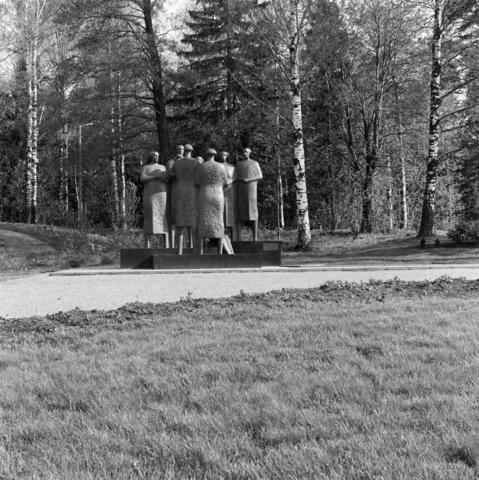 Antti Neuvosen Ystävät ja kylänmiehet -veistos Itäkeskuksessa. Tuoksessa seitsemän pronssista ihmishahmoa seisoo jalustalla tiiviinä ryhmänä. Taustalla Ystävyyden puiston viereistä metsää.
