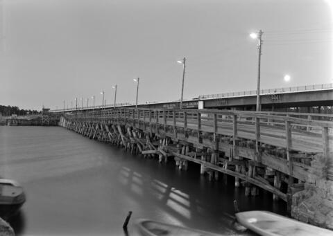 / Brändö broar fotograferade i kvällsskymning år 1957. I förgrunden den gamla bron i trä, i bakgrunden den nya betongbron under byggnad.  