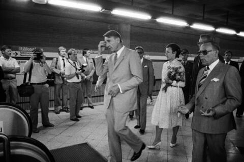 Presidentti Koivisto kävelee Itäkeskuksen metroaseman laiturilla Metrojohtaja Unto Valtasen vierellä. Taustalla presidentin puoliso Tellervo Koivisto kantaa kukkakimppua. Joukko toimittajia ottaa valokuvia.