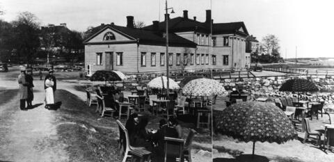 Kaivopuiston kylpylä kuvattuna vuonna 1935. Etualalla terassi, jolla aurinkovarjoin katettuja pöytiä. Yhdessä pöydässä istuu ryhmä naisia.