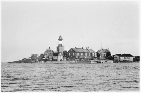 Mitt på bilden finns en fyr, som omges av lägre träbyggnader. I förgrunden finns en stor brygga.