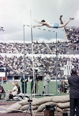 Stavhoppstävling på Olympiastadion. En idrottare på den högsta höjden av sitt hopp, efter att just ha överträtt ribban.