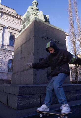 En ung pojke skejtar utanför Finlands Bank. Som underlag för sitt konststycke har han piedestalen till Snellmans staty.