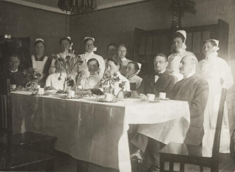 Ryhmä lääkäreitä ja hoitajia katetun kahvipöydän ääressä.