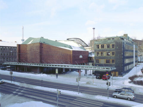 Kulttuuritalo, punatiilinen ja sen 5-kerroksinen toimistorakennus, vihertävän harmaata peltiä, talon takaa näkyy Linnanmäen vuoristorata, etualalla Sturenkatua.