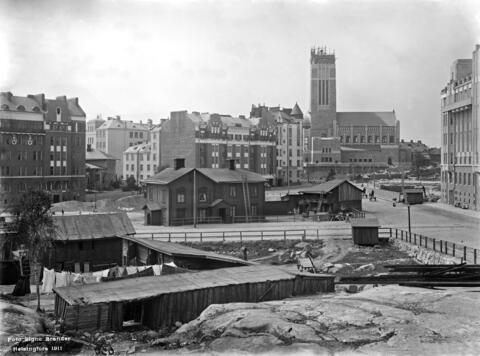 Etualalla kalliota ja puisia hökkeleitä Fleminginkadun varrella (Agrikolankatu 8 - Fleminginkatu 3). Oikealla menee Agrikolankatu, kivinen kerrostalo on Agrikolankatu 11. Keskellä, nykyisen Karhupuiston kohdalla on huvilarakennus, joka kuului Kaiun huvila-alueeseen (Kaiku 9). Taustalla vasemmalla Viides linja 12, 14, 16, 18 ja Kallion kirkon rakennustyömaa, Itäinen Pappikatu (=Itäinen Papinkatu 2)