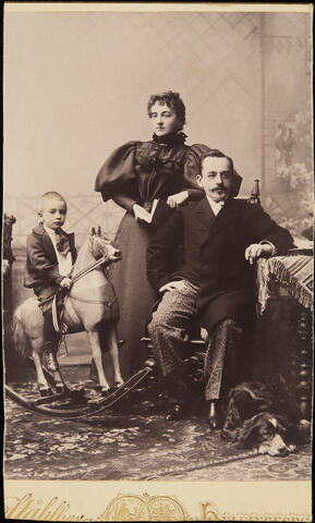 Constantin Grünberg (s. 1.5.1891) vanhempiensa Eugienie ja Constantin Grünbergin kanssa. Constantin on noin neljävuotias ja istuu keinuhevosen selässä. Isä Constantinin jaloissa makaa koira.
